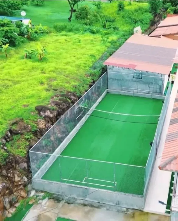 Cancha de deportes de grama sintética cercada, rodeada de vegetación verde.