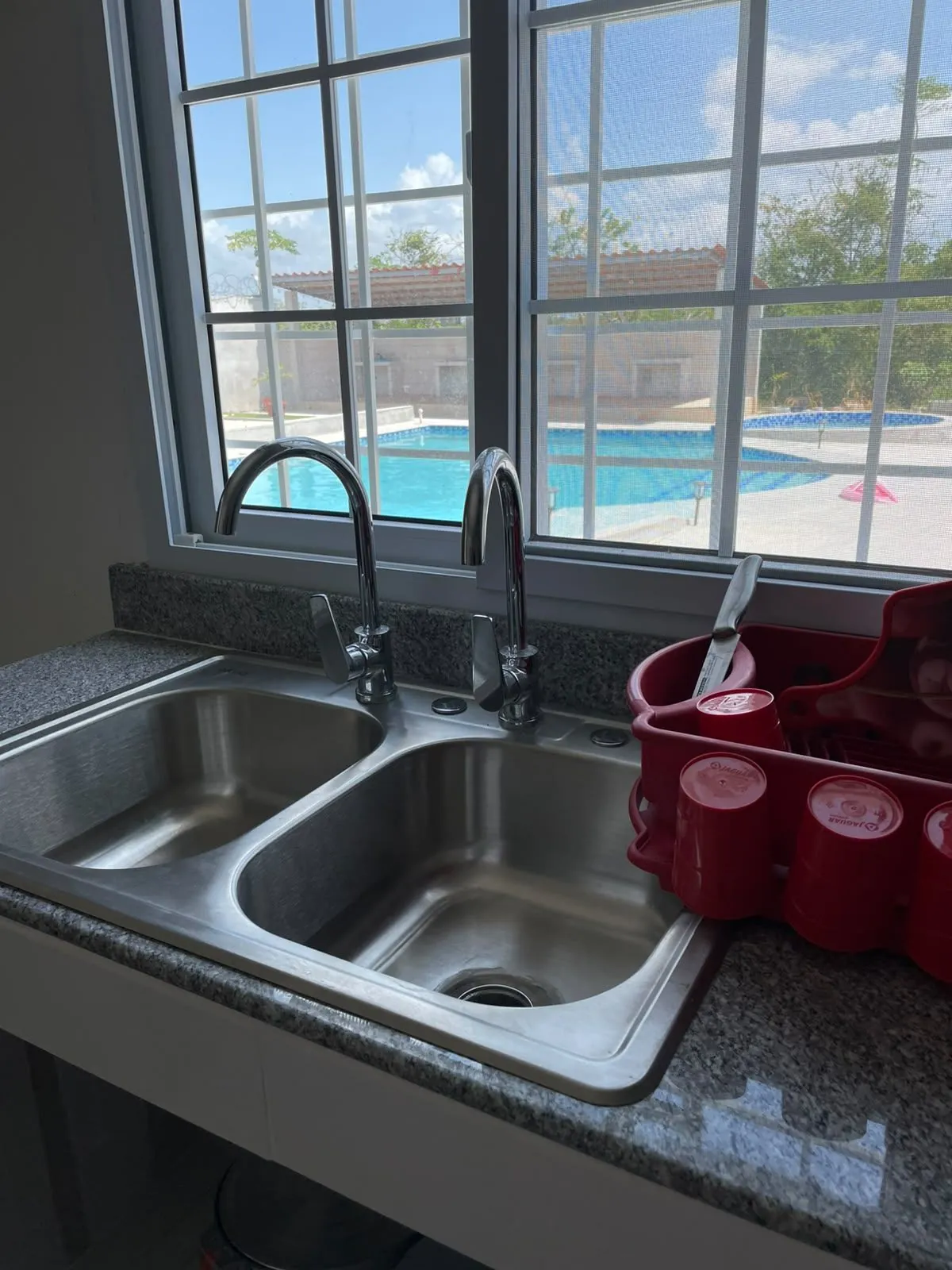 Fregadero de cocina frente a una ventana con vista directa a la piscina.
