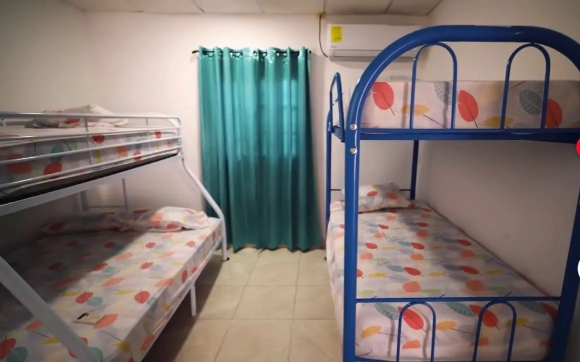 Habitación con dos literas metálicas, cortina turquesa y aire acondicionado.