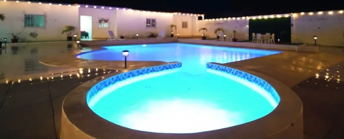 La piscina iluminada de azul por la noche con guirnaldas de luces alrededor del patio.