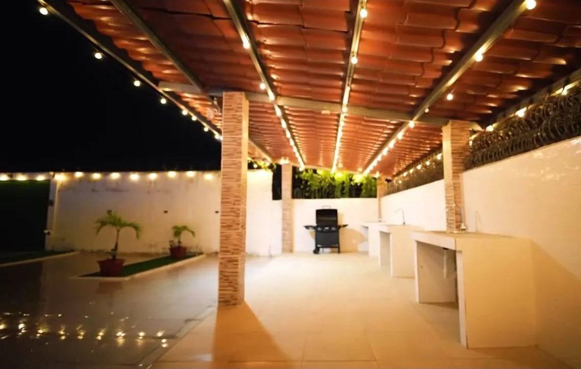 Gazebo techado iluminado de noche con asador y mesones de concreto.