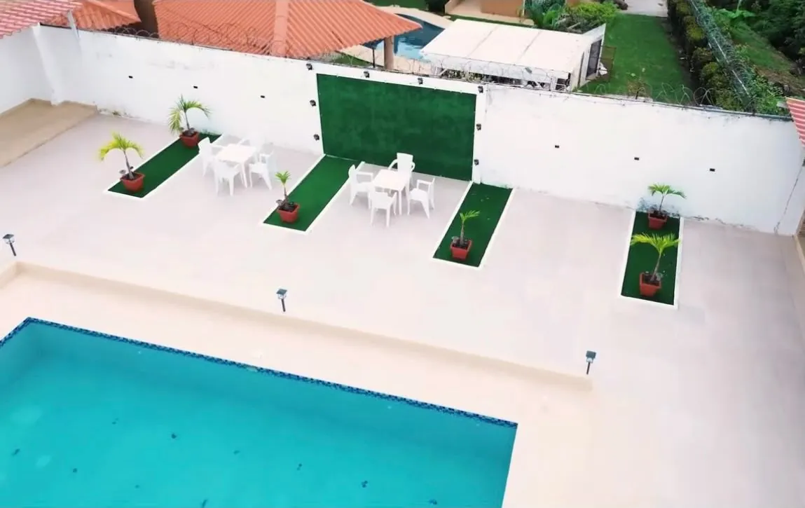 Área social junto a la piscina con mesas, sillas y palmeras en jardineras.